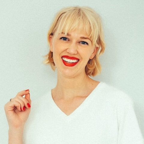  smiling woman with short blonde hair wearing a white top in front of a pale background.