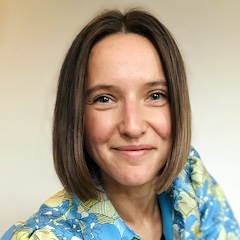 A smiling woman with a bob of shoulder-length straight hair wearing a colourful floral outfit.