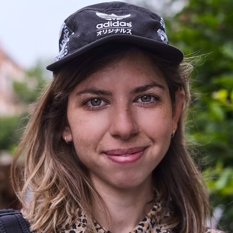 Close up of the face of a smiling woman wearing a baseball cap outdoors.