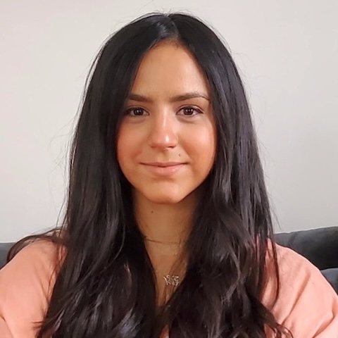 A woman with long dark hair sitting down looking directly at us.